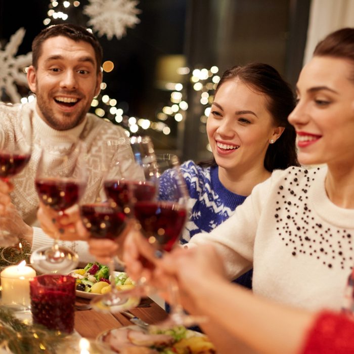 happy friends having christmas dinner at home, drinking red wine and clinking glasses