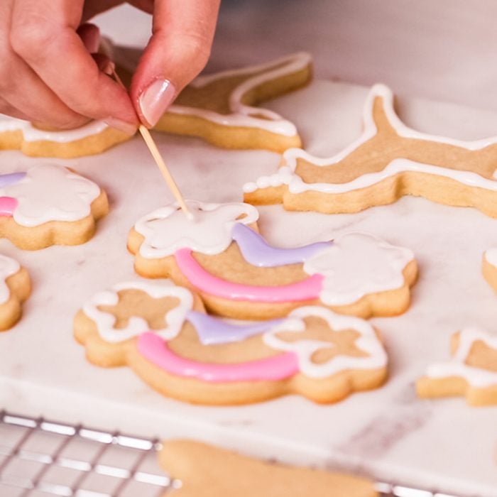 Decorating unocrn shaped sugar cookies with royal icing for little girl birthday party.