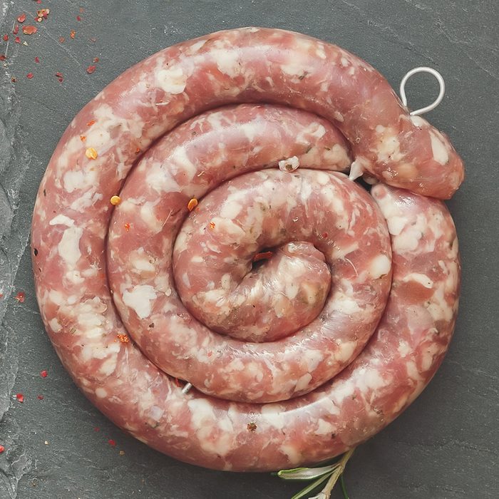 Raw uncooked gourmet sausages with rosemary with rosemary and spices on a rustic background. Overhead view, vintage toned image, blank space