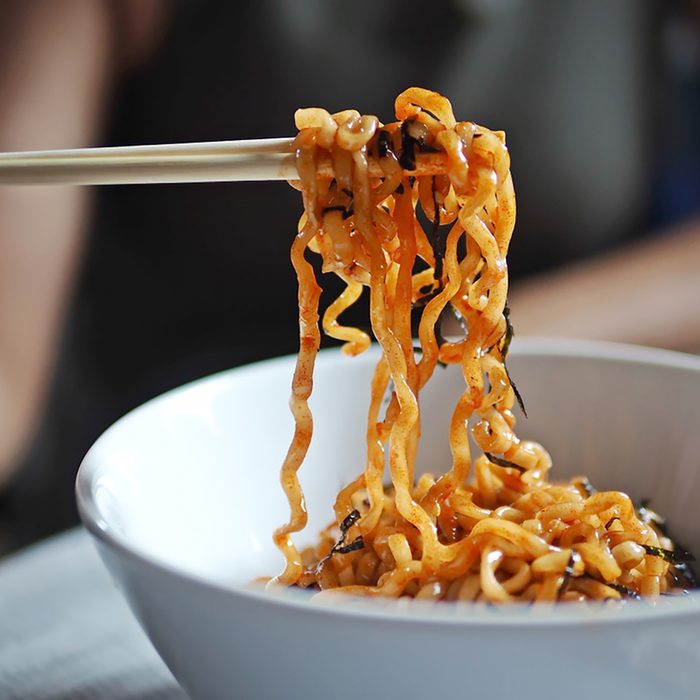 Woman eating instant noodles with wooden chopsticks on blurred background of her arms and body