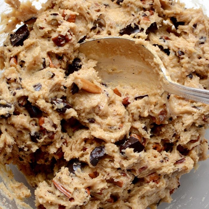 Raw cookie dough being mixed with chocolate chunks and chopped pecan nuts; Shutterstock ID 178109060; Job (TFH, TOH, RD, BNB, CWM, CM): Taste of Home