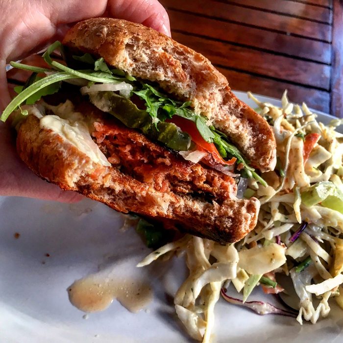 Vegan burger with pickles, tomato, and pickles on a whole wheat bun with a side of coleslaw