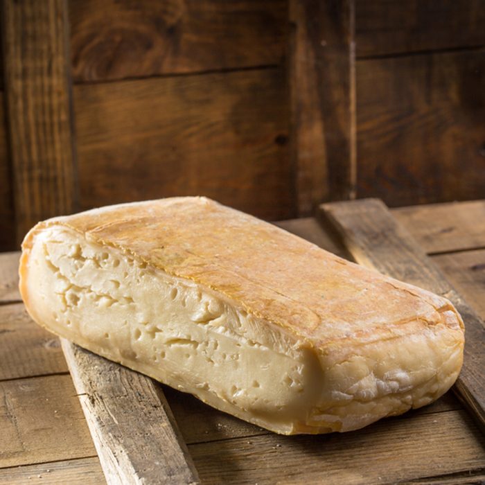 Piece of taleggio cheese on wooden board on dark background.