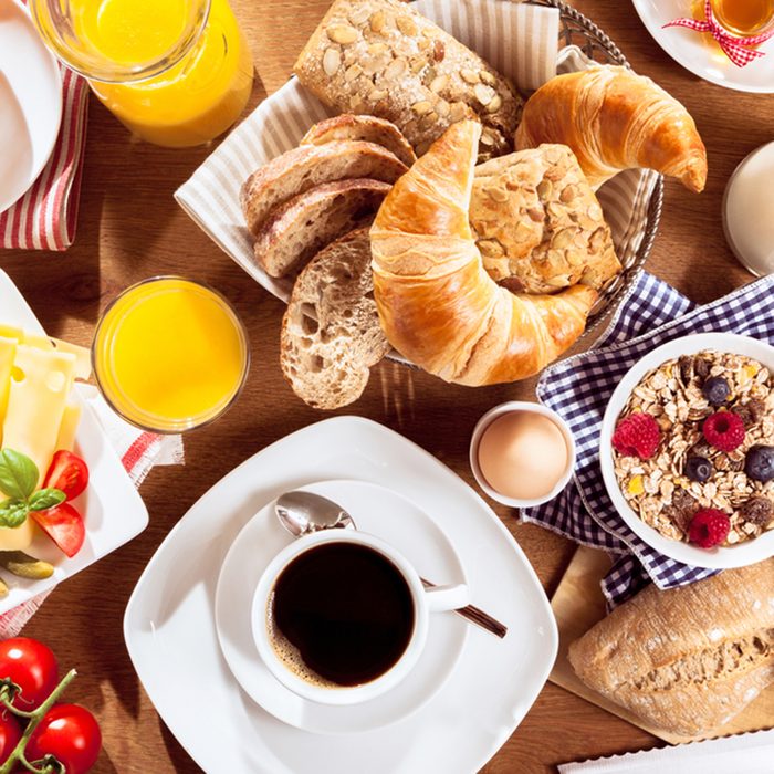 Top view of coffee, juice, fruit, bread and meat on table