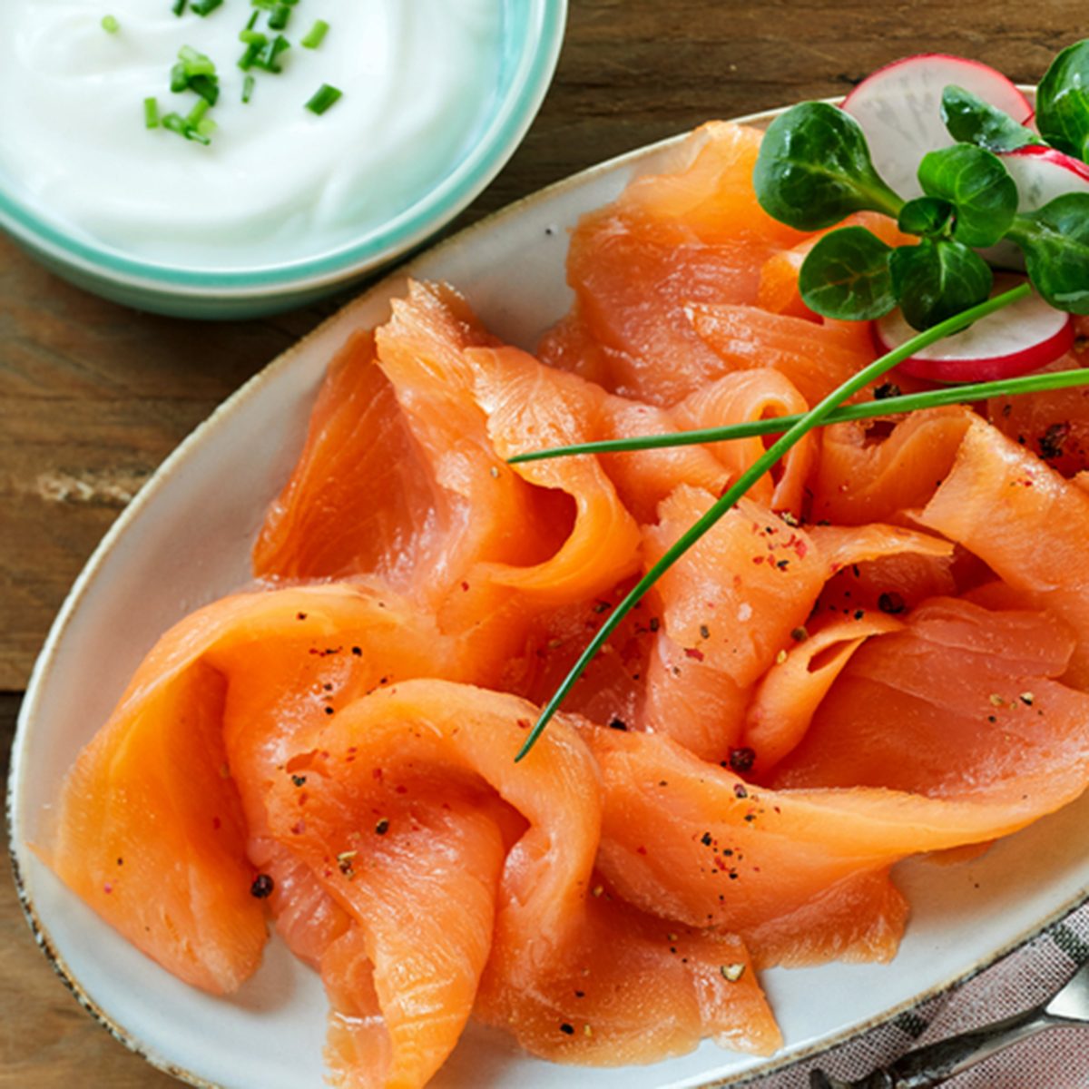 Fresh slices of healthy smoked salmon or lok served with a creamy chive sauce on an oval platter viewed from above on wood with copy space
