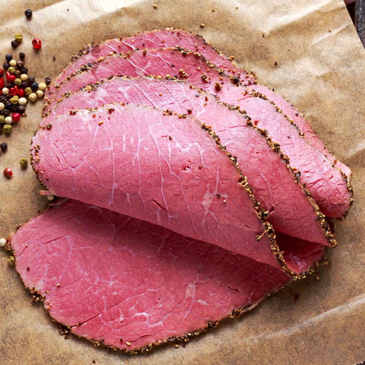 Peppered roast beef pastrami slices on paper with grains of coloured pepper.