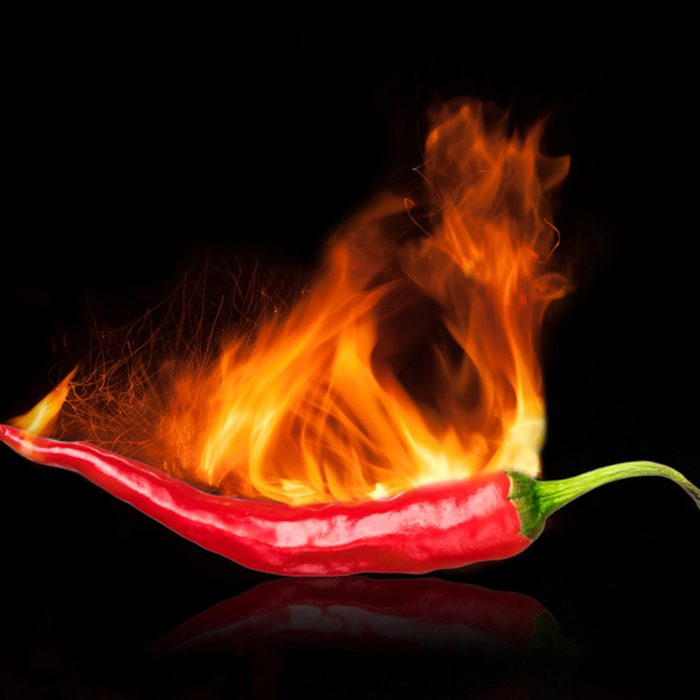single red chili peppers with fire on black background