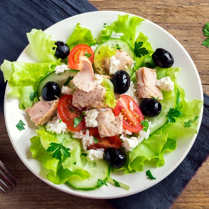 Tuna salad with tomatoes, black olives, rice, feta cheesse and greens on rustic wooden background with copy space