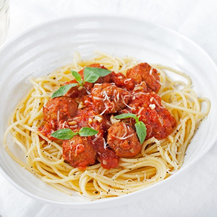 Meatballs in tomato sauce and fresh basil with spaghetti on a white background
