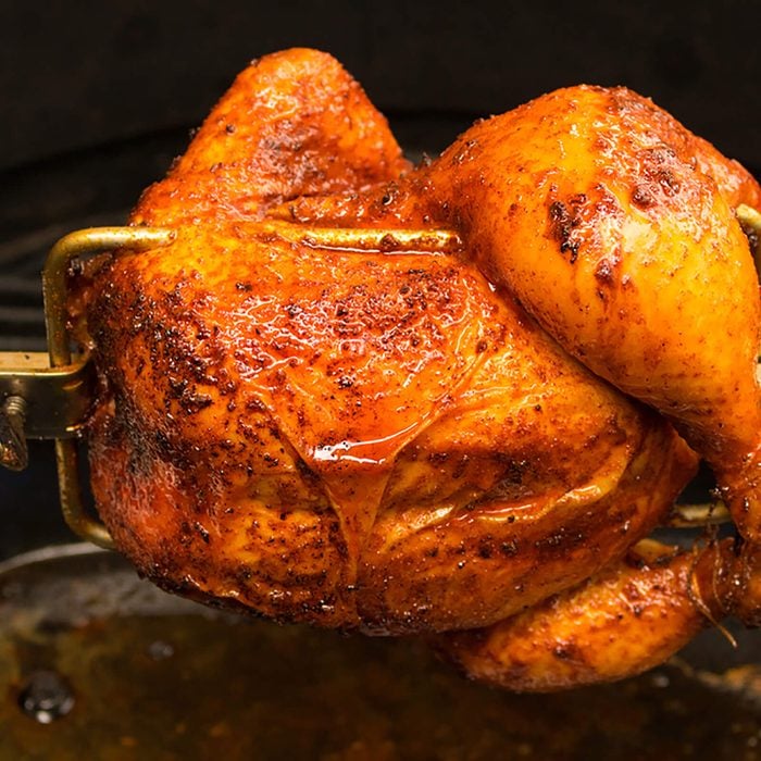 Charred rotisserie chicken over open flames in a barbecue.
