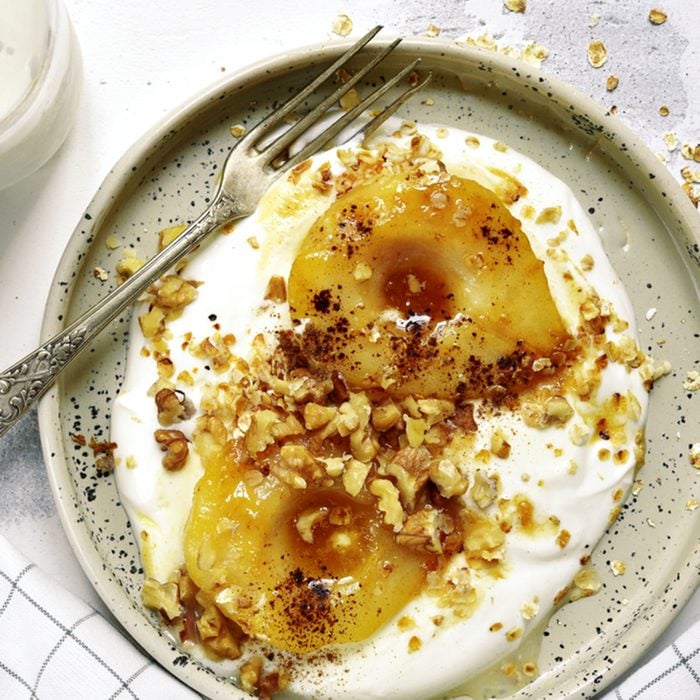 Caramelized pear with nuts and yogurt for a breakfast on a rustic craft plate over white slate