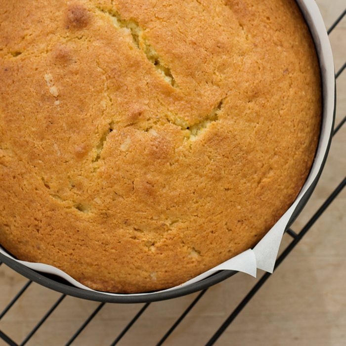 A round shaped Maderia cake in a baking tin on a wire, cooling rack.