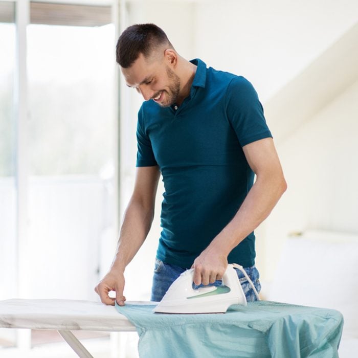 man ironing shirt on iron board at home