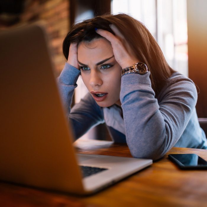 Frustrated worried young woman looks at laptop upset by bad news