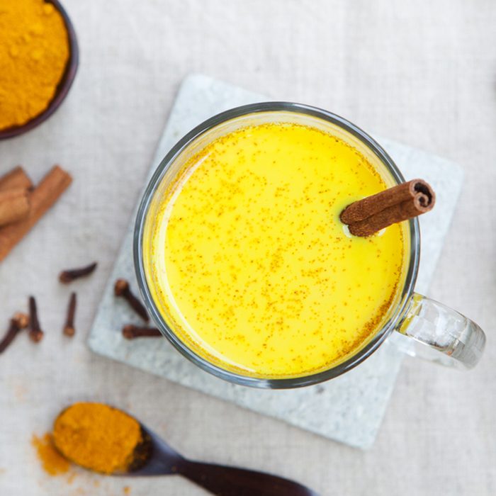 Turmeric drink, latte, tea, milk with cinnamon in a glass mug with fresh and dried turmeric on a textile grey background.