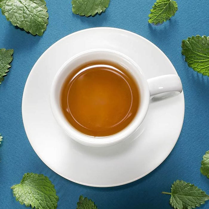 White cup of mint tea with fresh meant leaves on blue background.