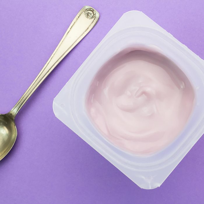 Healthy strawberry fruit flavored yogurt with natural coloring in plastic cup isolated on purple background with small silver spoon - top view