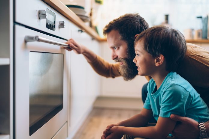 Father And Son Cooking Dinner At Home With Clean Oven Glass