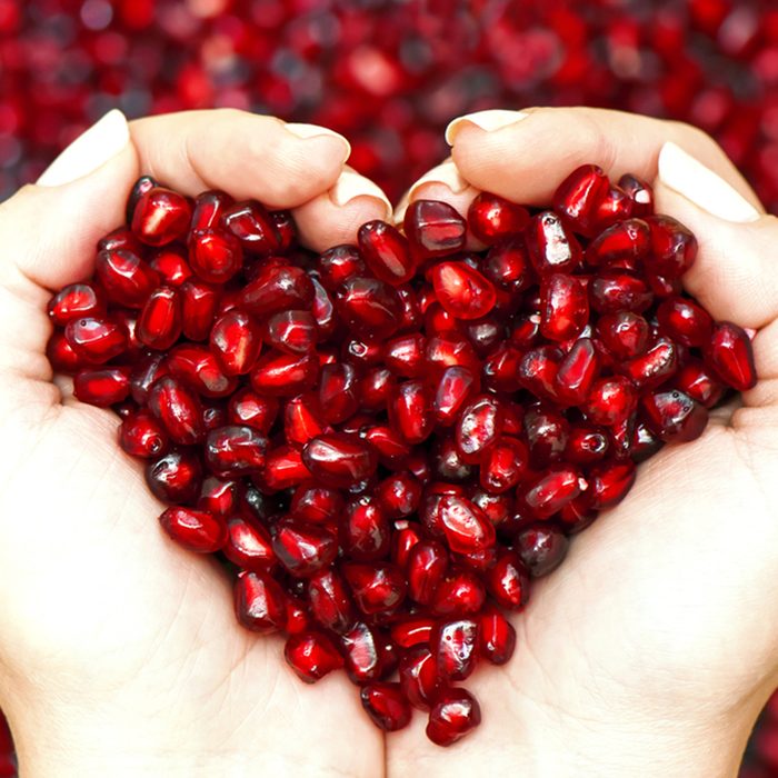 Pomegranate seeds in woman hands shaping heart symbol