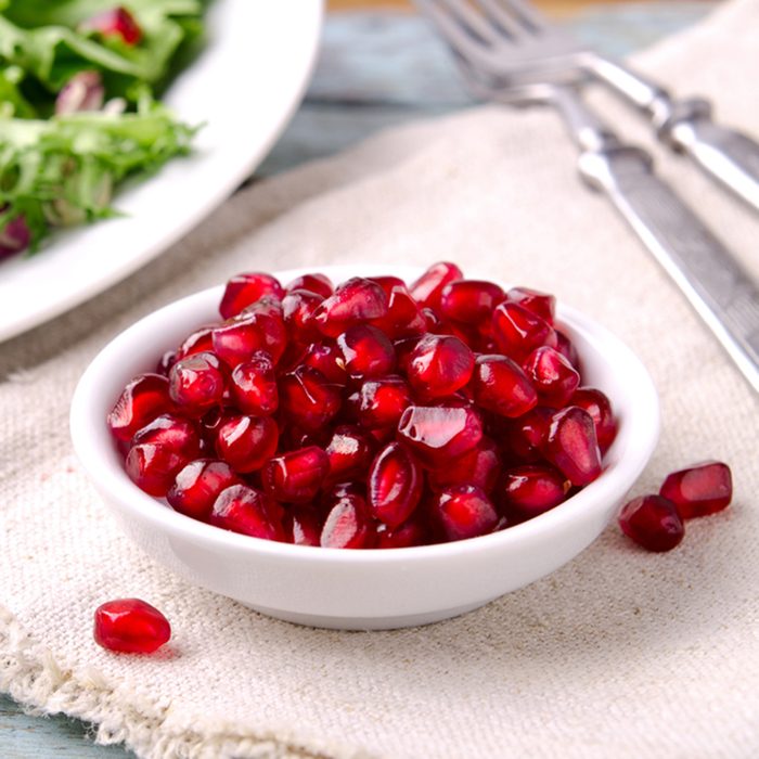 Green salad with spinach, frisee, arugula, radicchio and pomegranate seeds on blue wooden background.