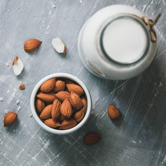 Top view of the almond milk in the glass bottle with almond nuts in the white bowl on the grey table.