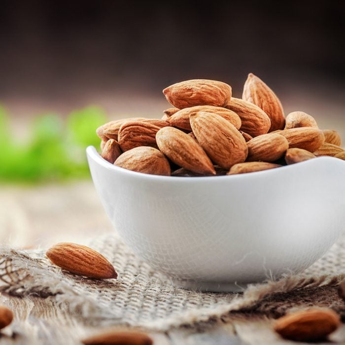 Almonds in white porcelain bowl on wooden table.