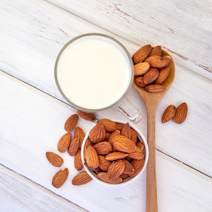 Close up top view of healthy almond milk in drinking glass with seed in white cup and wooden spoon on white wooden table plate 