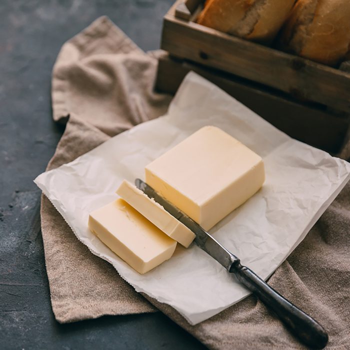 Pat of fresh farm butter with a knife and bread over rustic background