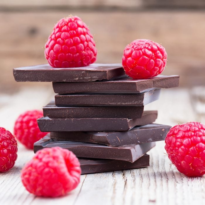 Dark chocolate stack with fresh raspberries, on wooden table.