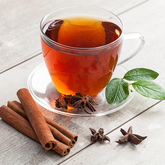 Glass cup of tea with cinnamon on rustic table.