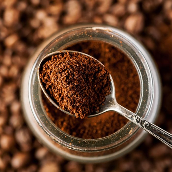 Ground coffee in a metal spoon on a top of glass jar, shallow depth of field