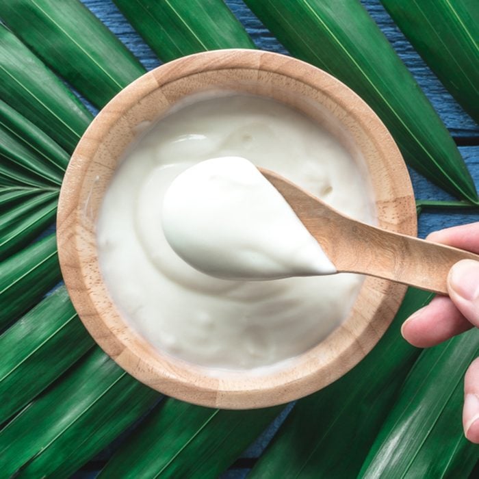 Top view of yogurt in wooden bowl on green leaves background