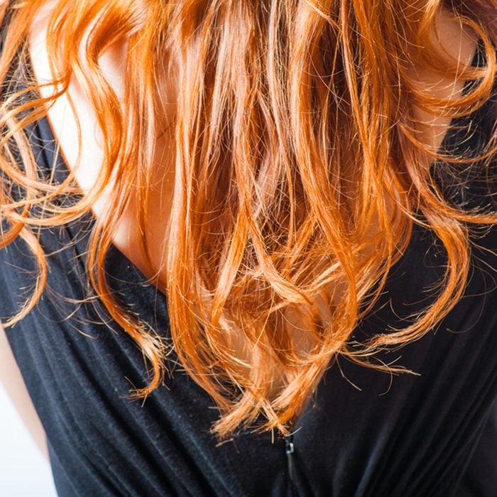 rear closeup view of the shoulders of red haired (carrot-top) female weared black dress