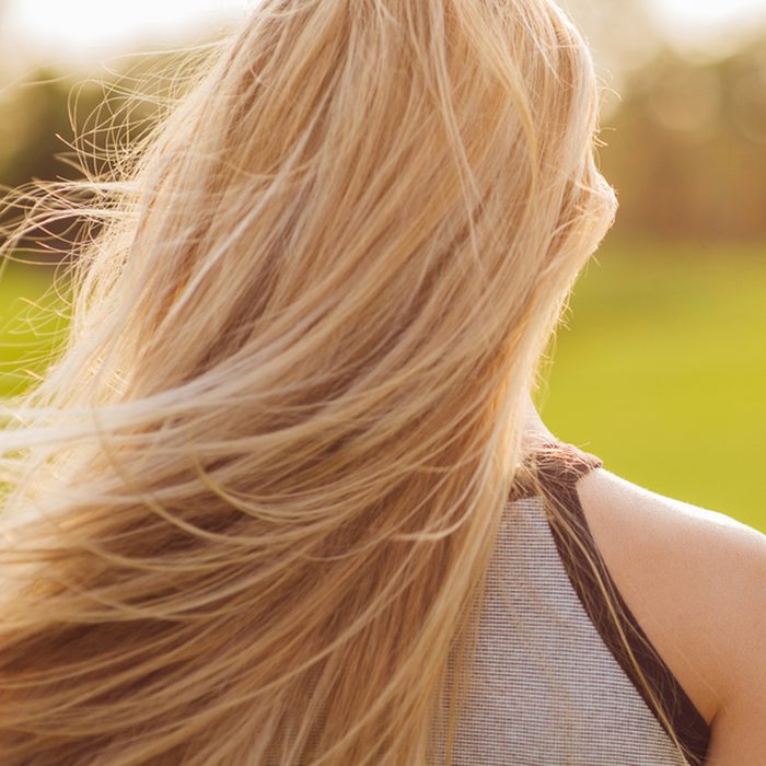 Beautiful young woman with long blonde hair in motion turned back, at sunset time on the green golf field.