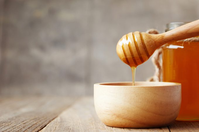 Honey and wooden honey dipper on wooden background.