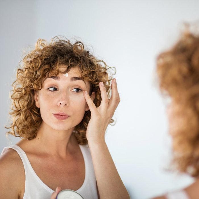young curly woman using skin cream on in a mirror