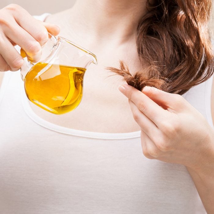 Unrecognizable woman applying oil mask to hair tips in a bathroom