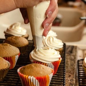 Female hands holding piping bag filled with cream cheese frosting decorating cupcakes