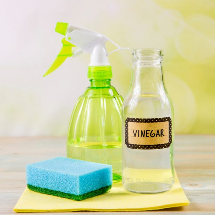 Chemical free home cleaner products concept. Using natural destilled white vinegar in spray bottle to remove stains. Tools on wooden table, green bokeh background, copy space.; Shutterstock ID 1296110344; Job (TFH, TOH, RD, BNB, CWM, CM): TOH