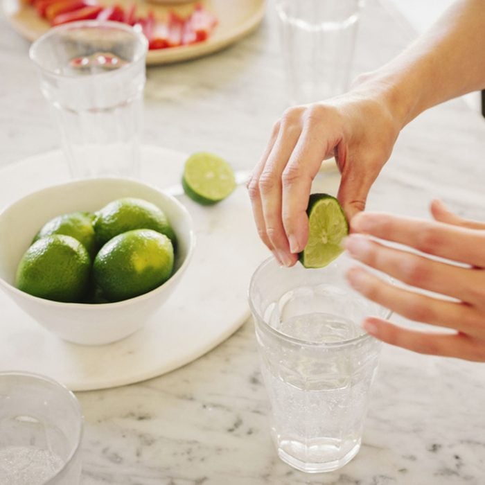 A woman squeezing fresh limes into a glass of water; Shutterstock ID 604753493; Job (TFH, TOH, RD, BNB, CWM, CM): Taste of Home