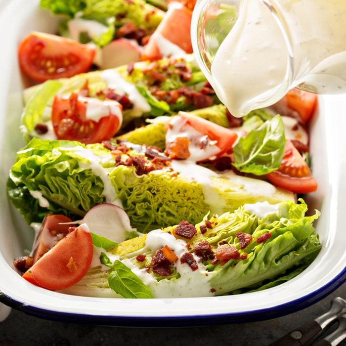 Wedge salad with baby lettuce, cherry tomatoes, bacon and ranch dressing pouring over.;