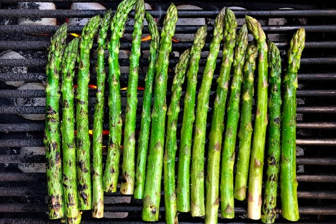 Spears of asparagus on a charcoal grill.