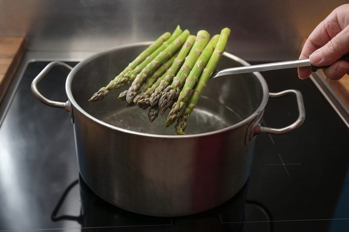 A person holding a pile of asparagus over a boiling pot of water.