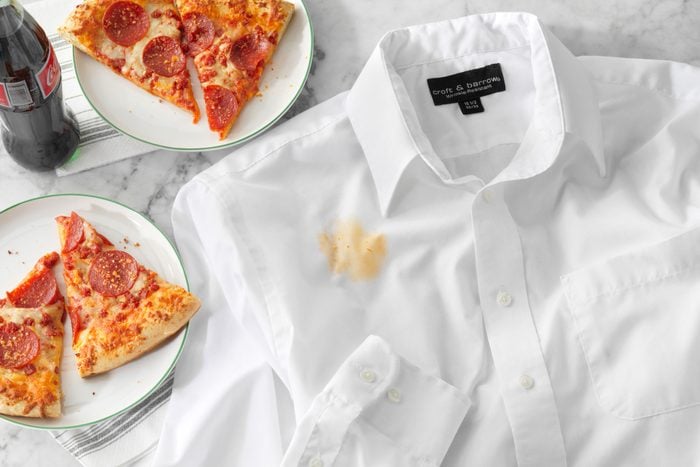 White Shirt Stained With Pizza Grease with slices of pizza and soda nearby; all on a marble kitchen counter top