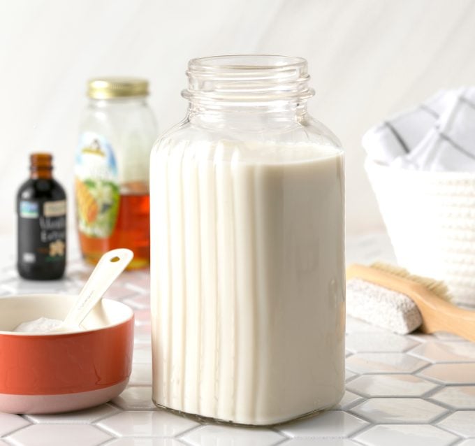 A bottle of milk, honey, vanilla and a dish of baking soda ready to combine for a soothing milk foot bath.