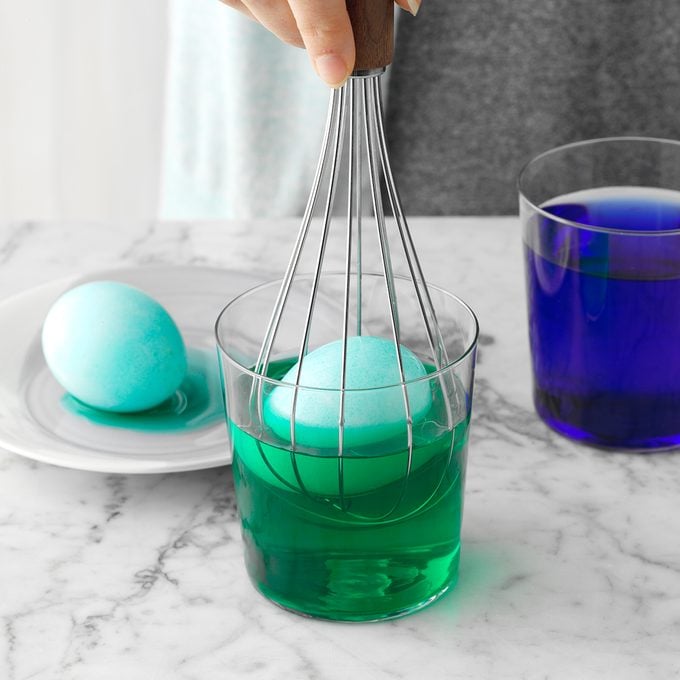 person using a whisk to dip an egg into a cup of dye