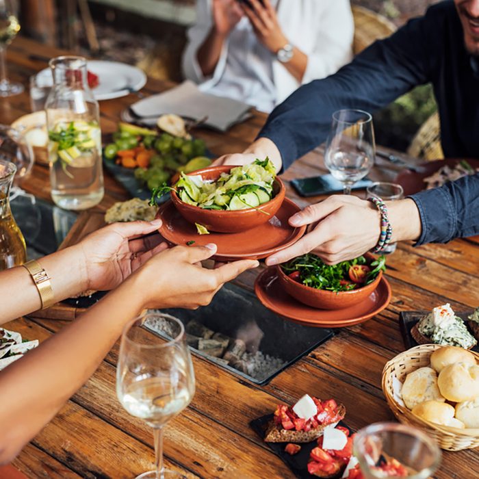 Hands of cropped unrecognisable woman and man passing salad bowl at vegetarian restaurant.