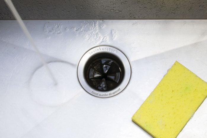 garbage disposal in a stainless steel sink with water running and yellow sponge nearby