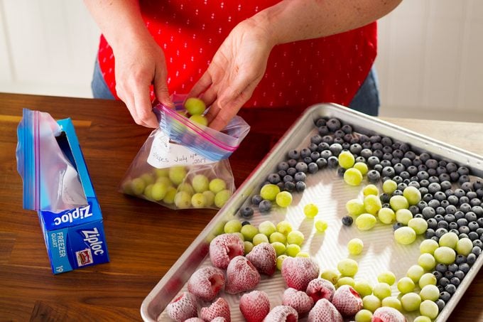 A person putting frozen berries and grapes into a freezer bag.