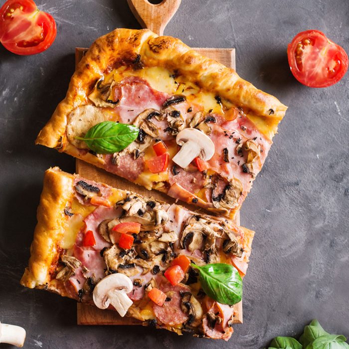 a slice of square pizza with basil tomatoes and mushrooms on a wooden board.